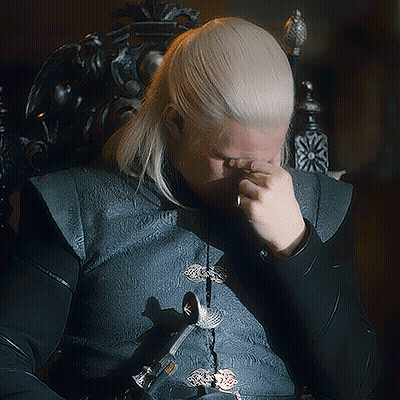 A Man With Blonde Hair Is Sitting In A Chair And Covering His Face With His Hand GIF