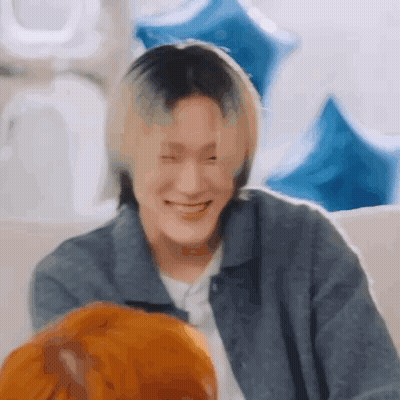 A Man With Blonde Hair Is Smiling While Sitting On A Couch With Balloons In The Background . GIF