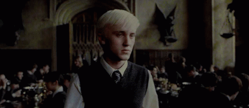 A Man With Blonde Hair Is Standing In A Room With A Crowd Of People . GIF