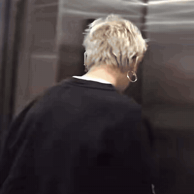 A Man With Blonde Hair Is Standing In An Elevator Wearing Hoop Earrings . GIF
