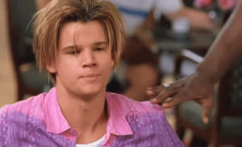 A Man With Blonde Hair Is Wearing A Pink Shirt And A Purple Shirt While A Woman Holds His Hand . GIF