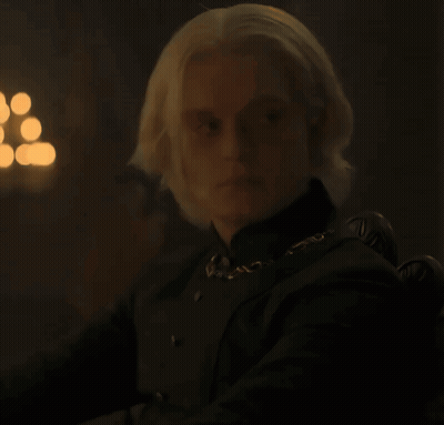 A Man With Blonde Hair Wearing A Black Shirt And A Gold Chain Around His Neck GIF