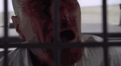A Man With Blood On His Face Is Behind Bars In A Cell . GIF