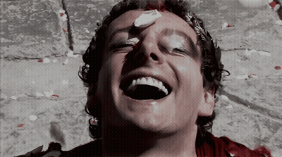 A Man With Blood On His Face Is Laughing With Petals Falling Around Him GIF