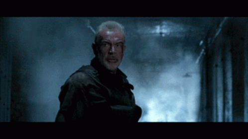 A Man With Blood On His Face Is Standing In A Dark Room GIF