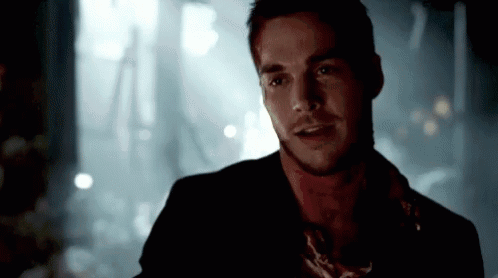 A Man With Blood On His Neck Is Standing In A Dark Room And Talking To Someone . GIF