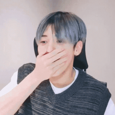 A Man With Blue Hair Is Covering His Mouth With His Hand While Wearing A Sweater Vest . GIF