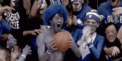 A Man With Blue Paint On His Face Is Holding A Basketball In Front Of A Crowd Of People Wearing Duke Shirts GIF