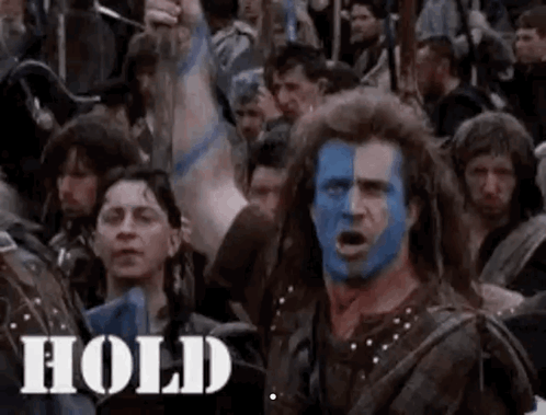 A Man With Blue Paint On His Face Is Standing In Front Of A Crowd Of People With Their Arms In The Air . GIF