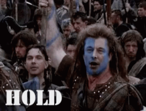 A Man With Blue Paint On His Face Is Surrounded By A Crowd Of People . GIF