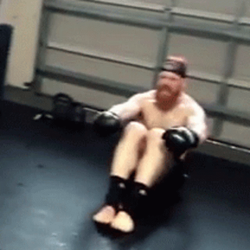 A Man With Boxing Gloves Is Sitting On A Black Mat GIF