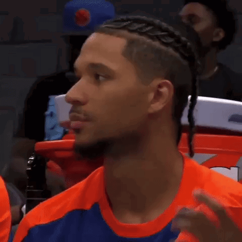A Man With Braids In His Hair Is Wearing An Orange Shirt And Sitting In The Stands . GIF
