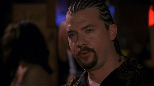 A Man With Braids On His Hair And A Beard Looks At The Camera GIF