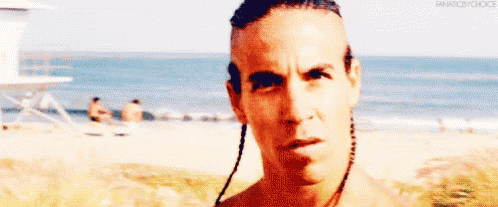 A Man With Braids On His Head Is Standing On A Beach . GIF