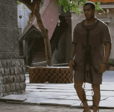 A Man With Chains Around His Legs Is Walking Down A Street GIF