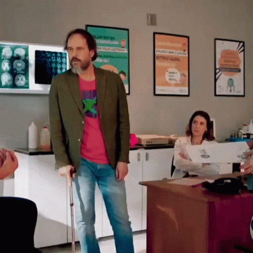 A Man With Crutches Is Standing In A Room With Posters On The Wall Including One That Says ' A ' On It GIF
