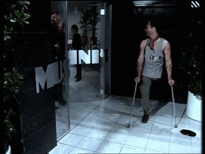 A Man With Crutches Is Walking In Front Of A Building That Says Mini GIF