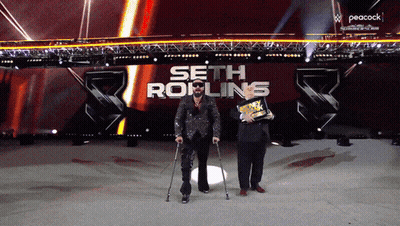 A Man With Crutches Stands In Front Of A Peacock Logo GIF