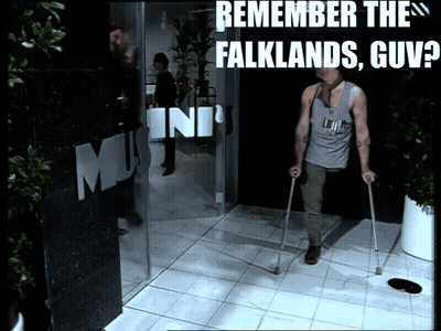 A Man With Crutches Walks In Front Of A Sign That Says Remember The Falklands GIF