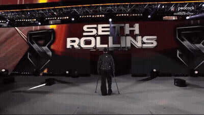 A Man With Crutches Walks On A Stage In Front Of A Sign That Says Seth Rollins GIF