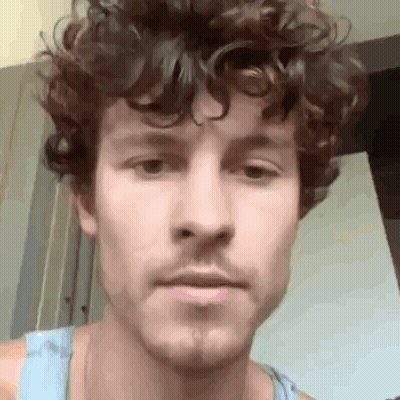 A Man With Curly Hair And A Beard Is Looking At The Camera . GIF
