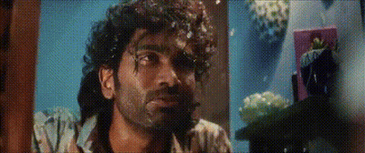 A Man With Curly Hair And A Beard Is Looking At The Camera In A Room . GIF
