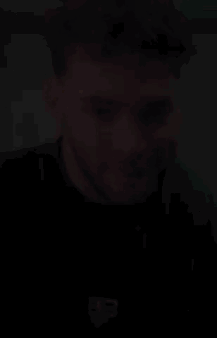 A Man With Curly Hair And A Beard Is Smiling And Wearing A Black T-Shirt . GIF
