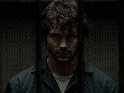 A Man With Curly Hair And A Beard Is Standing In A Dark Room GIF
