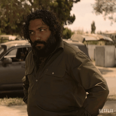 A Man With Curly Hair And A Beard Is Standing In Front Of A Netflix Logo GIF