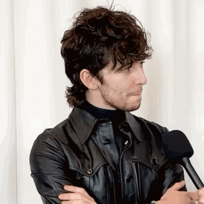 A Man With Curly Hair And A Beard Is Talking Into A Microphone . GIF
