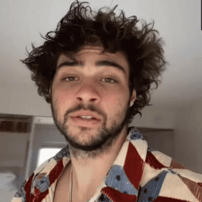A Man With Curly Hair And A Beard Is Wearing A Colorful Shirt And Making A Funny Face . GIF