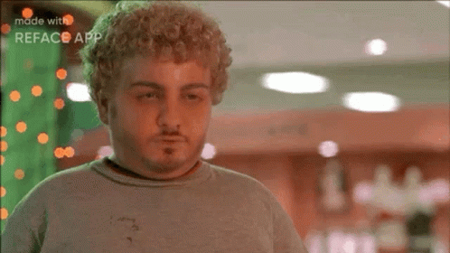 A Man With Curly Hair And A Beard Is Wearing A Grey Shirt And Looking Down . GIF