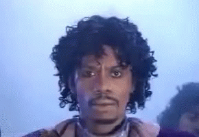 A Man With Curly Hair And A Beard Is Wearing A Purple Jacket . GIF