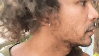 A Man With Curly Hair And A Beard Is Wearing A Ring In His Ear . GIF