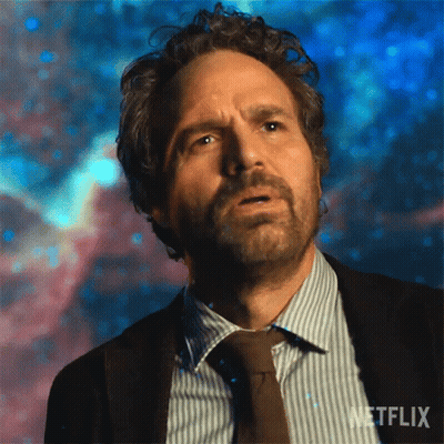 A Man With Curly Hair And A Beard Is Wearing A Suit And Tie And Looking Up At The Sky . GIF
