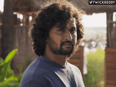 A Man With Curly Hair And A Beard Looks At The Camera With A Twitter Icon Above Him That Says 7Wickreddy GIF