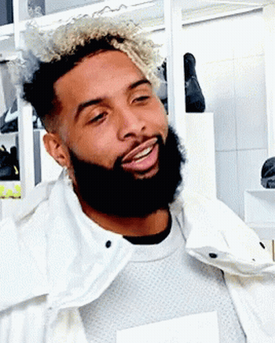A Man With Curly Hair And A Beard Wearing A White Jacket GIF