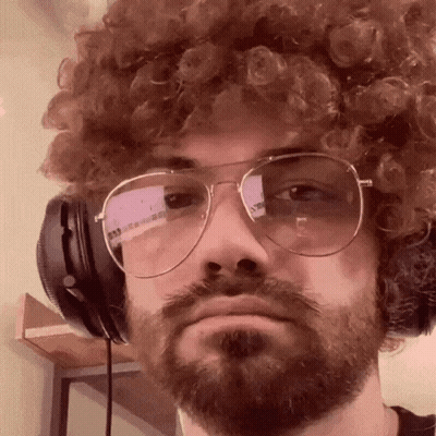 A Man With Curly Hair And A Beard Wearing Headphones And Glasses GIF