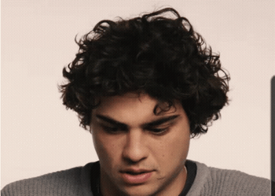 A Man With Curly Hair And A Gray Sweater GIF