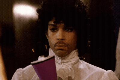 A Man With Curly Hair And A Mustache Holds A Purple Cup In His Hand GIF