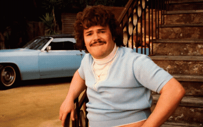 A Man With Curly Hair And A Mustache Is Leaning On A Railing With A Blue Car In The Background GIF