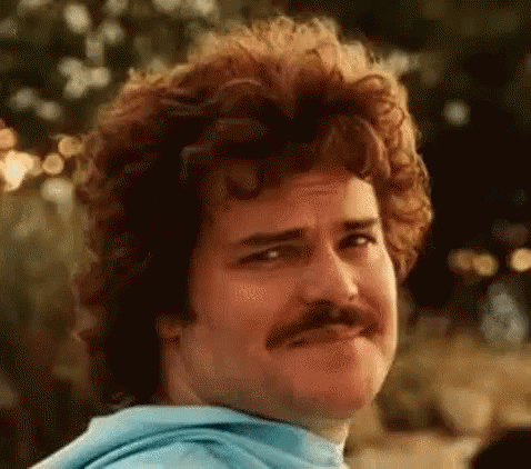 A Man With Curly Hair And A Mustache Is Looking At The Camera . GIF