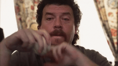 A Man With Curly Hair And A Mustache Is Sitting In Front Of A Window Holding Something In His Hands . GIF