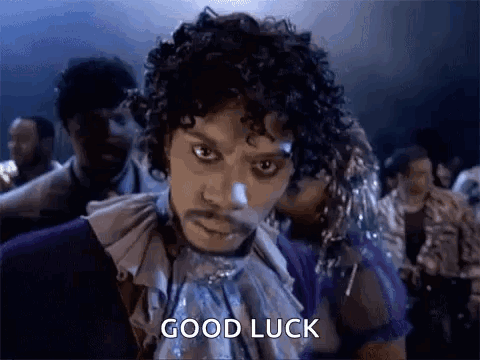 A Man With Curly Hair And A Mustache Is Standing In Front Of A Crowd Of People . GIF