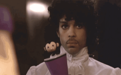 A Man With Curly Hair And A Mustache Is Wearing A Purple Shirt GIF