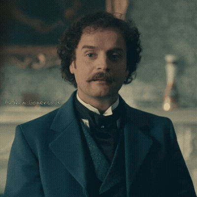 A Man With Curly Hair And A Mustache Is Wearing A Suit And Tie GIF