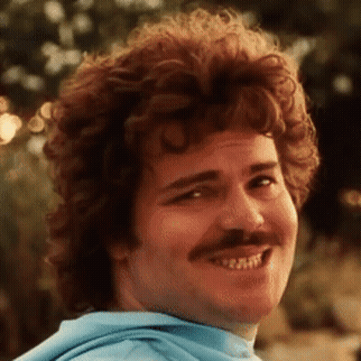 A Man With Curly Hair And A Mustache Smiles GIF