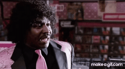 A Man With Curly Hair And A Pink Tie Is Sitting In A Chair In A Store . GIF