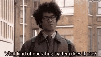 A Man With Curly Hair And Glasses Is Standing In Front Of A Building And Asking What Kind Of Operating System Does It Us GIF