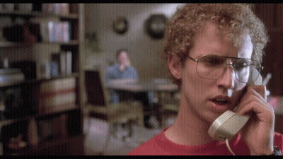 A Man With Curly Hair And Glasses Is Talking On A Phone GIF